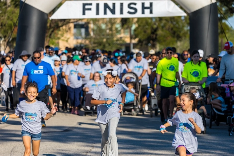 Three race participants smile at the camera during the race, with other participants in the background.