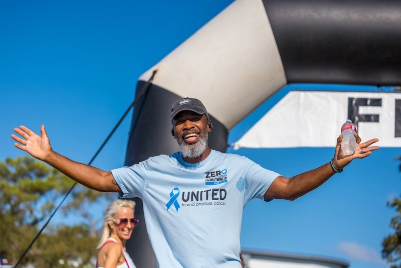 A female race participant smiles at the camera wearing a shirt that says, ‘Prostate Cancer Awareness Support Squad’.